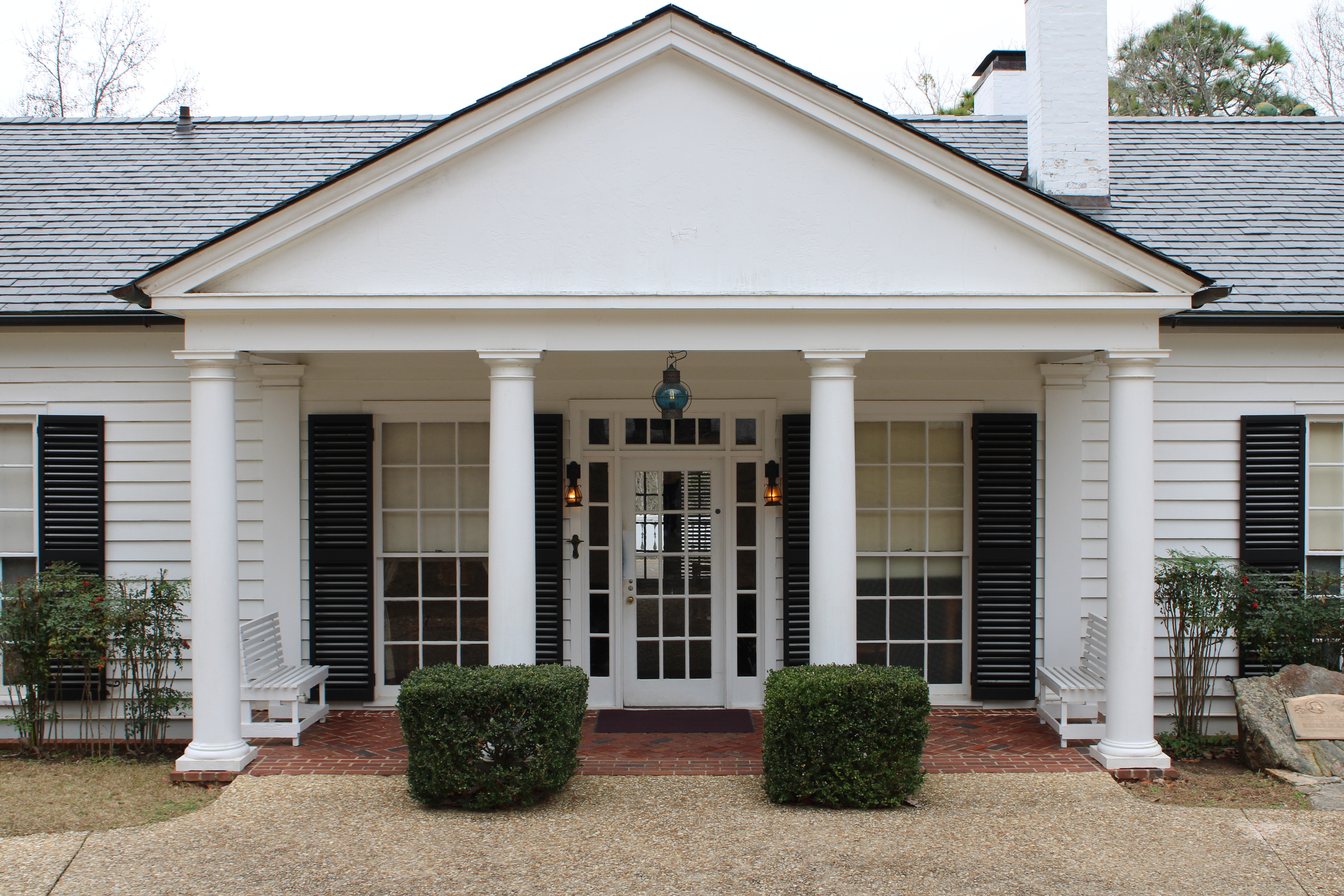 An up-close view of the main cottage, featuring a front outdoor foyer with white benches, large windows with black shutters, and the main door